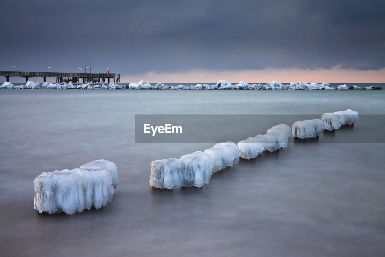 Frozen wooden posts on sea against cloudy sky