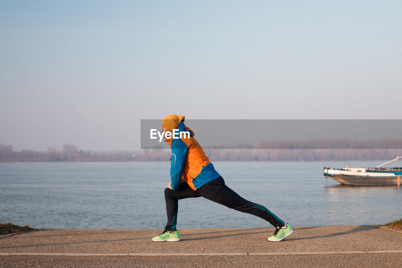 Mid adult man stretching by river during sunset