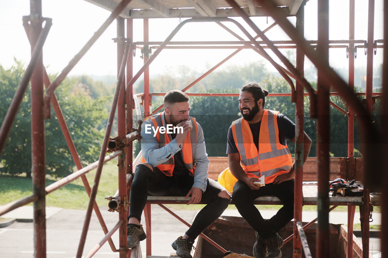 Smiling workers talking while sitting on built structure