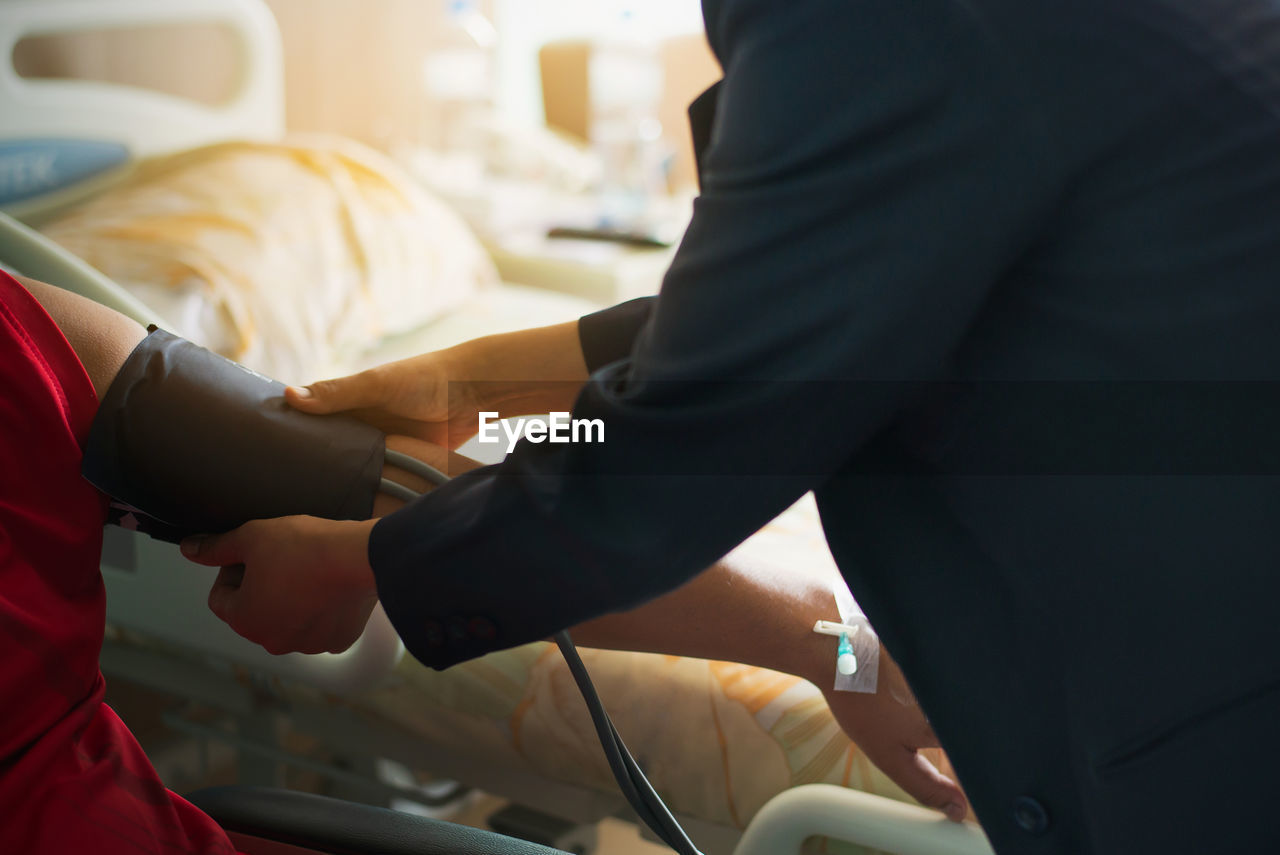 Midsection of female doctor checking blood pressure of male patient in hospital