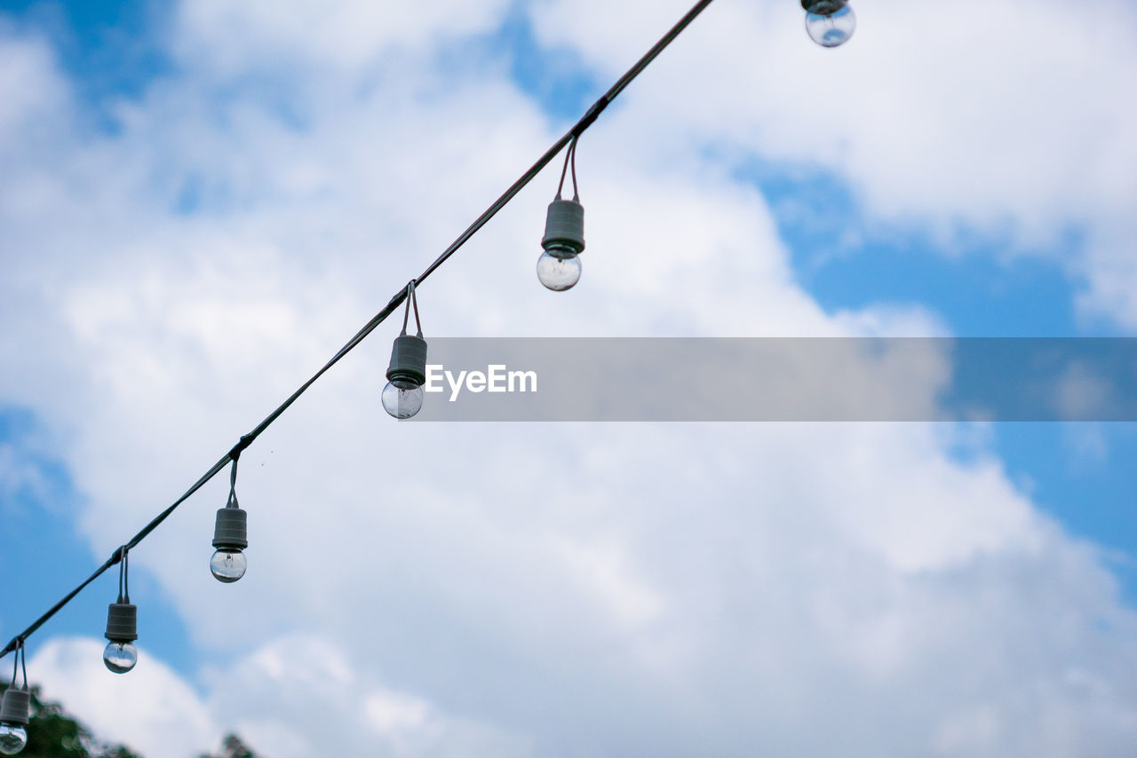 Low angle view of light bulbs hanging against sky