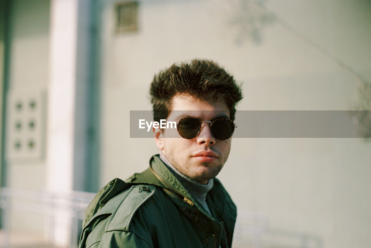 Portrait of young man wearing sunglasses against wall