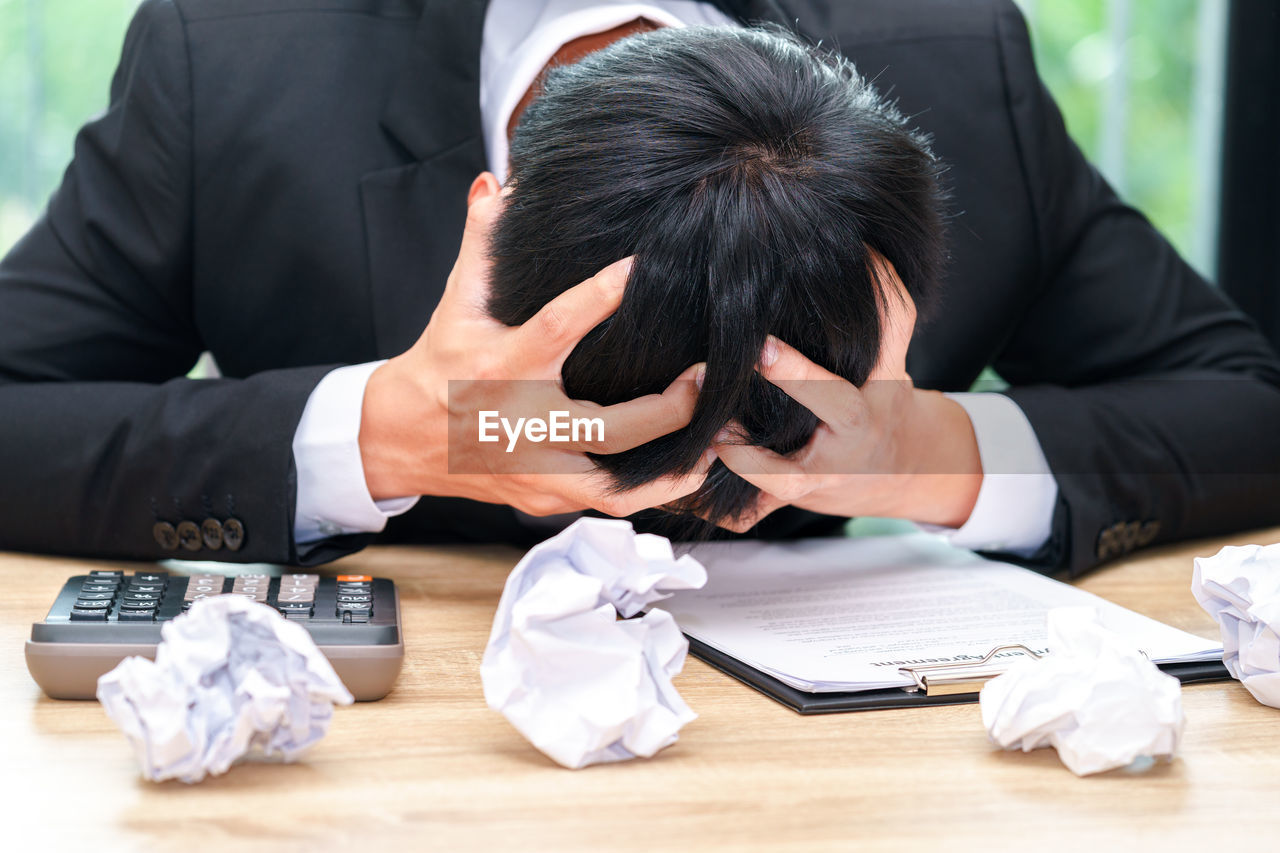 Close-up of tensed businessman by crumpled papers on desk