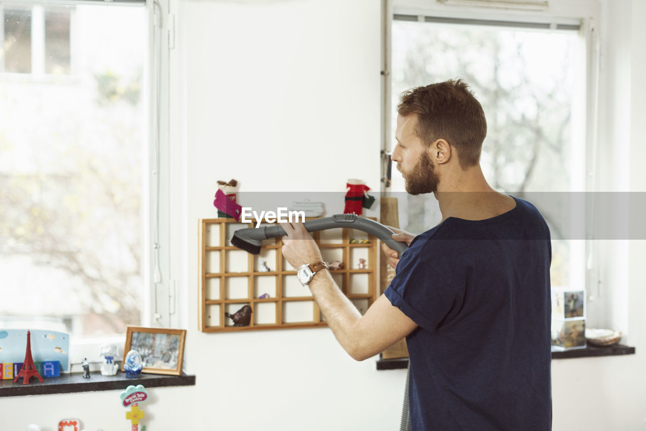 Young man vacuuming small shelves at home