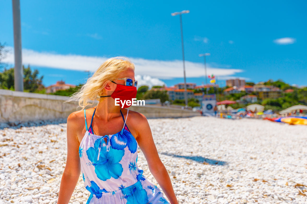 Woman wearing mask looking away while standing at beach