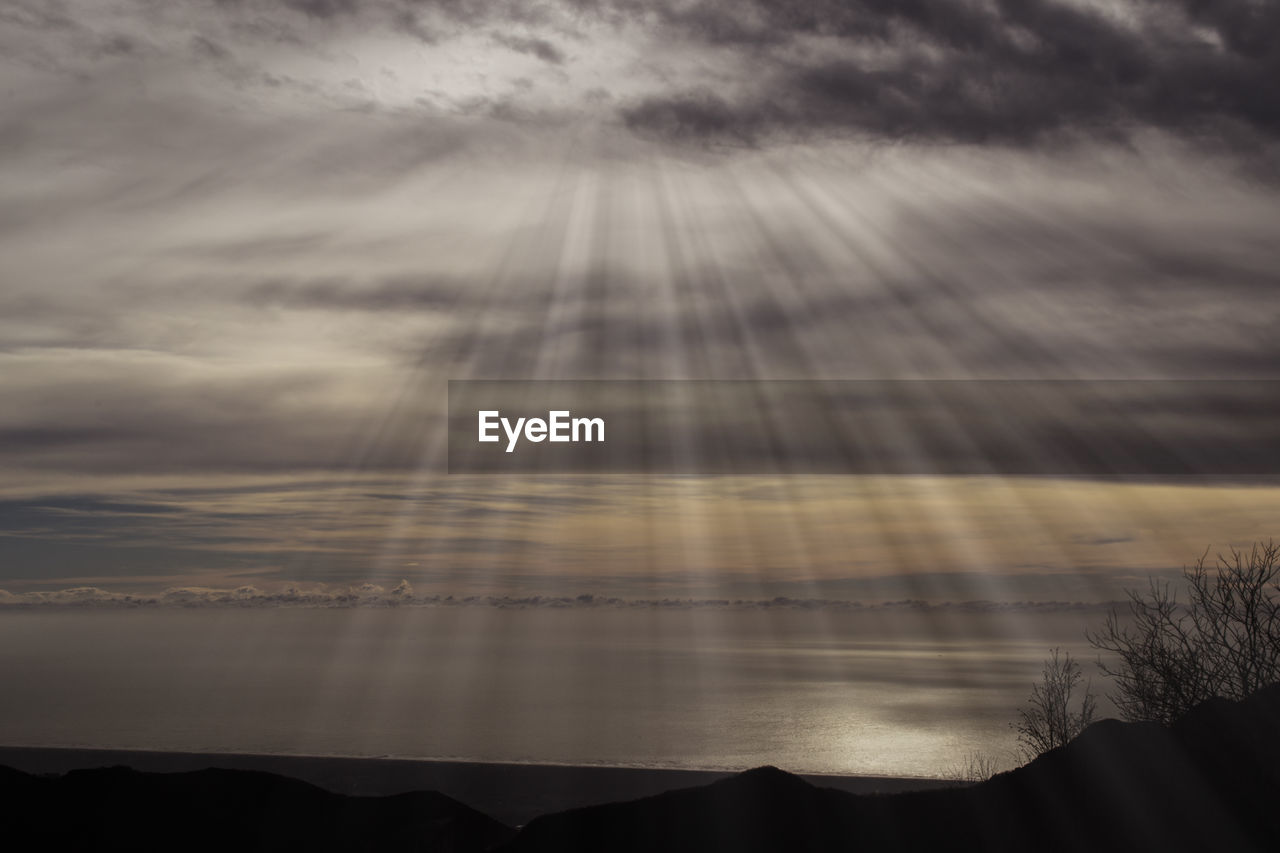 Idyllic shot of sunbeam through clouds in sea during sunset