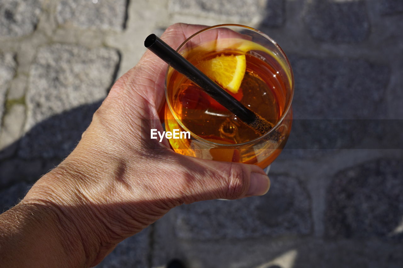 Cropped image of hand holding aperol spritz on footpath