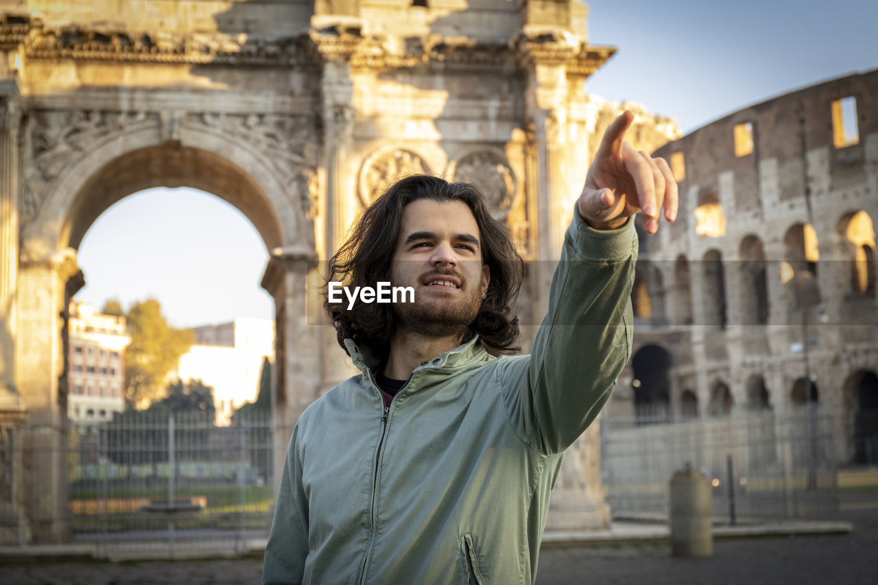 Young smiling man poses for a photo in front of the arch of titus.he is pointing the right direction