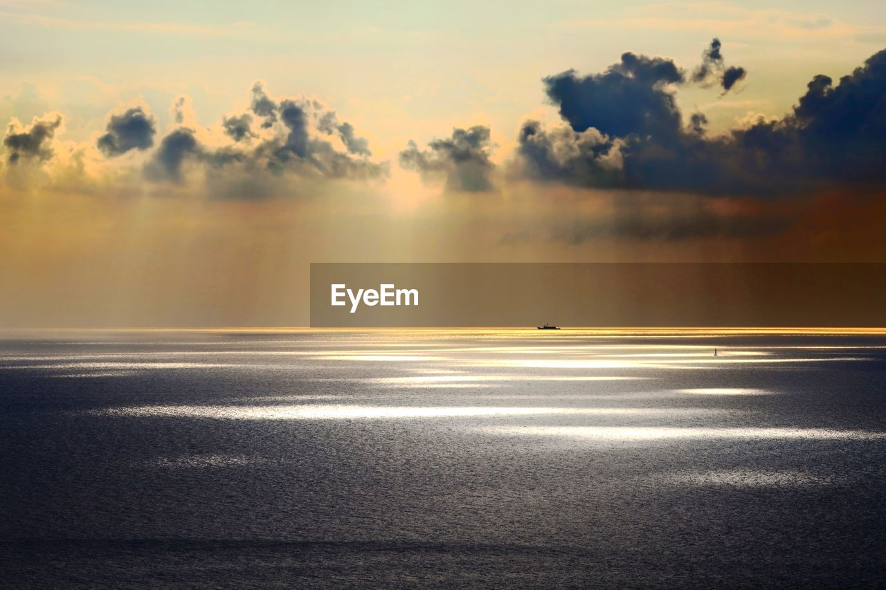 Scenic view at sunset with spots of light seeping into the sea with a ship on the golden horizon