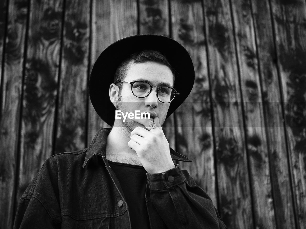 Young man wearing eyeglasses and hat against wooden wall