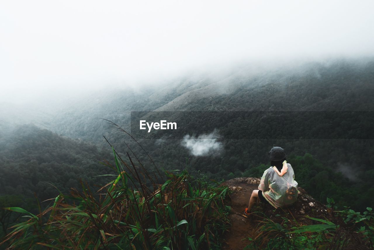 Rear view of person sitting on mountain against foggy weather