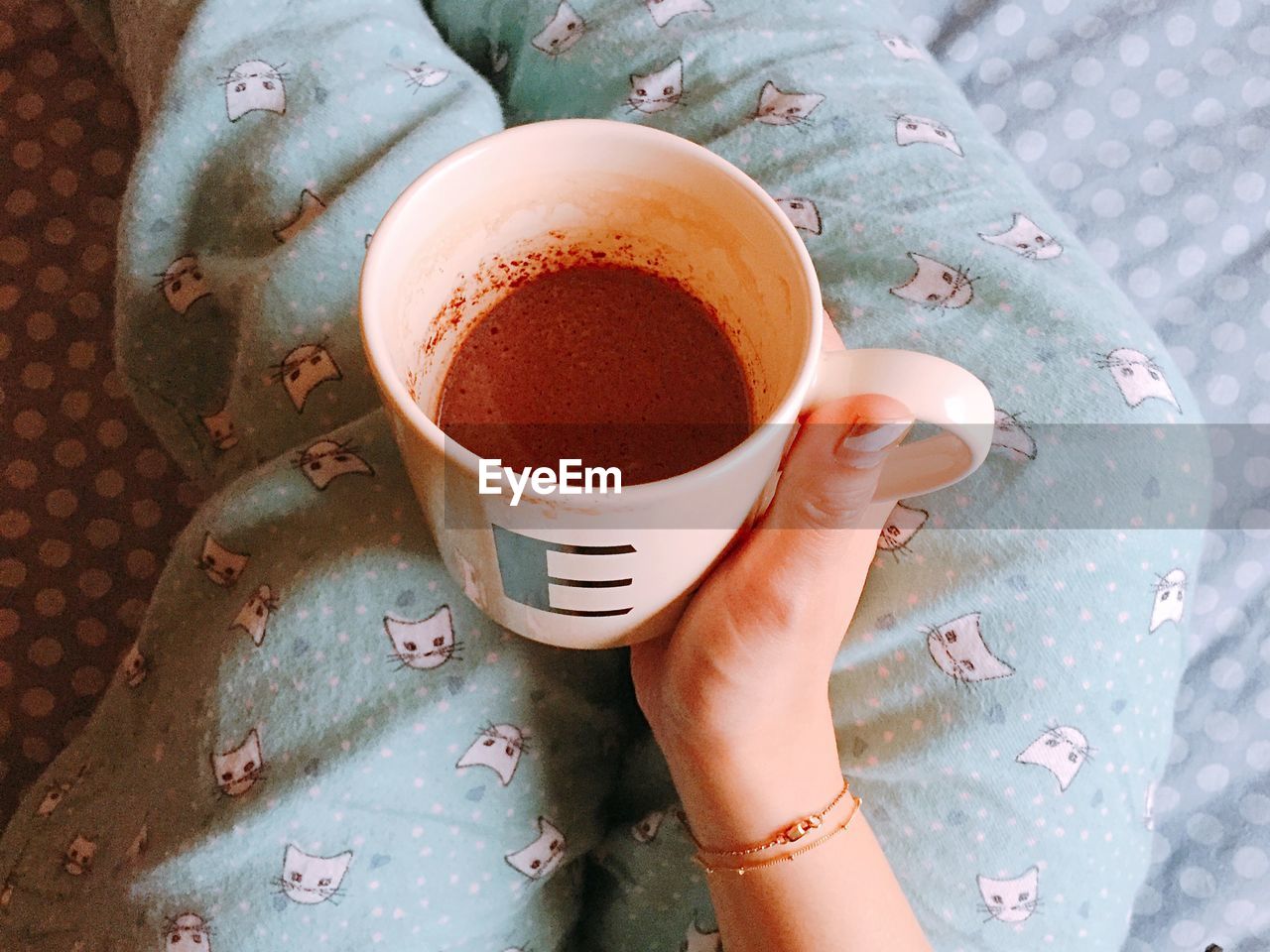 Midsection of woman holding hot chocolate in mug on bed