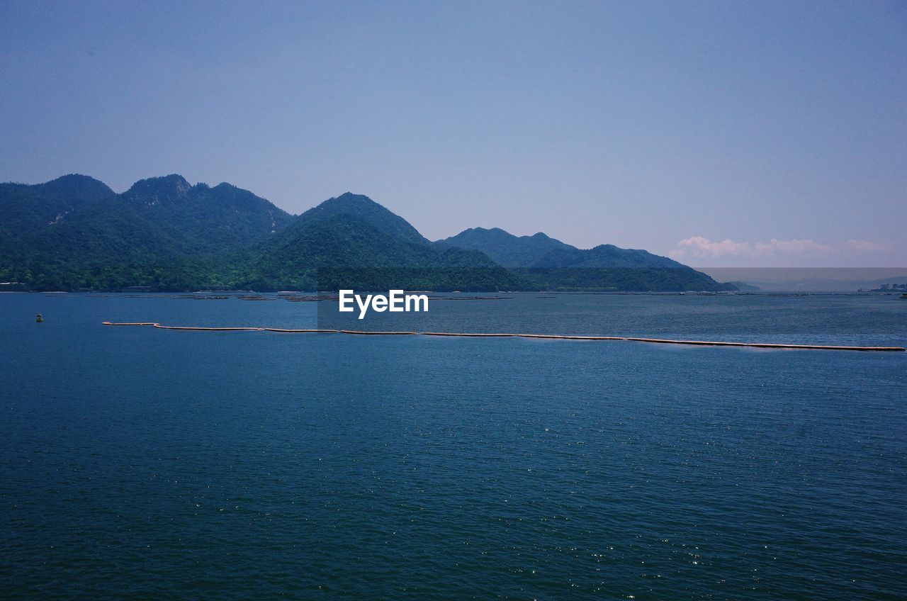 SCENIC VIEW OF SEA AND MOUNTAINS AGAINST BLUE SKY
