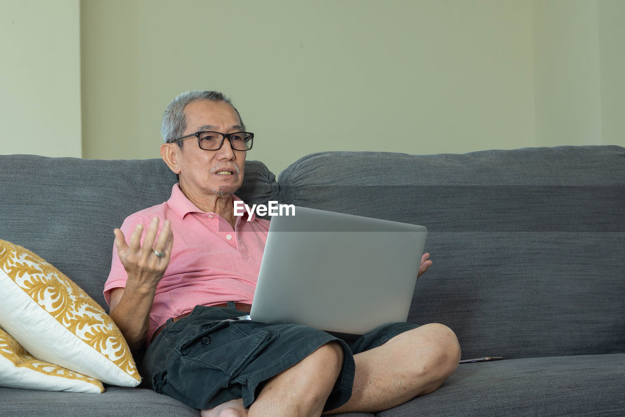 YOUNG MAN USING MOBILE PHONE WHILE SITTING ON SOFA