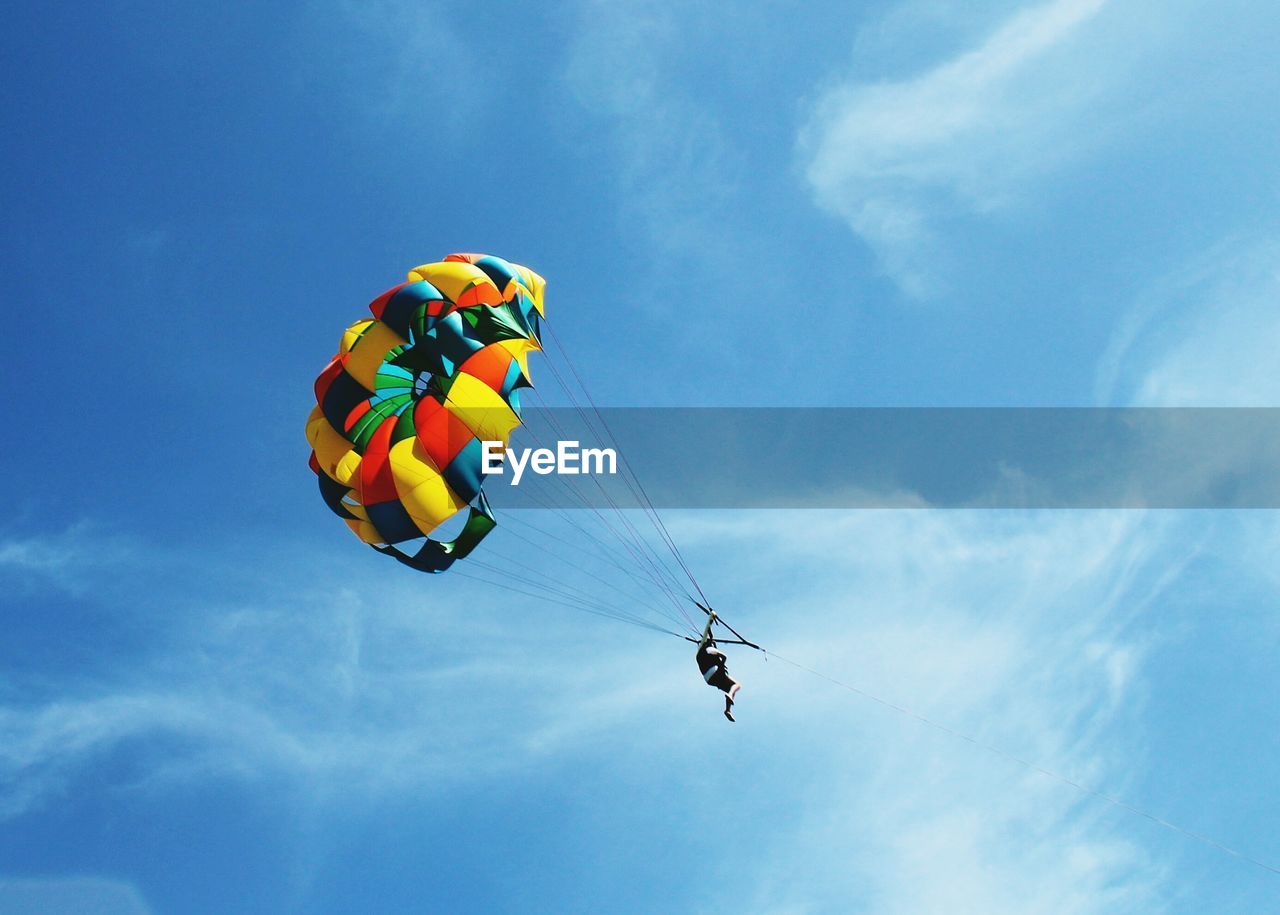 Low angle view of man parasailing against blue sky