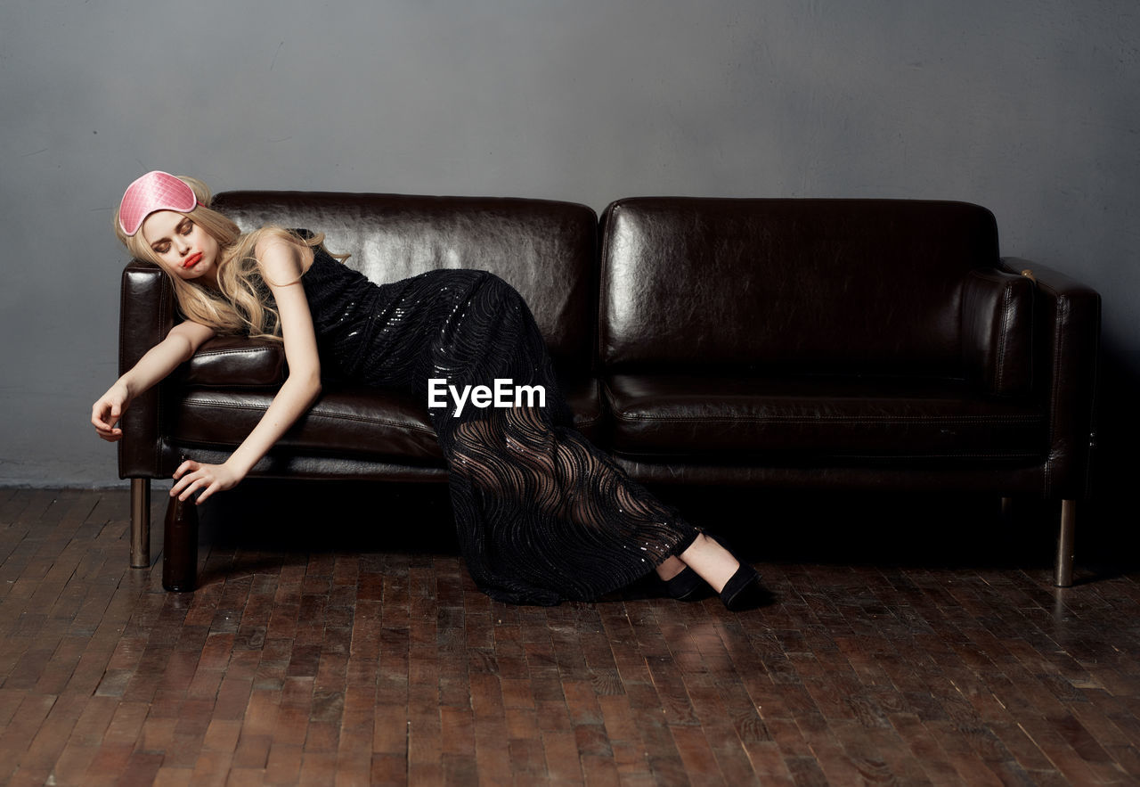 YOUNG WOMAN SITTING ON SOFA AGAINST WALL AT HOME