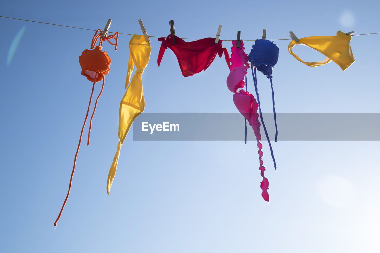 Low angle view of colorful female swimwear hanging against the blue sky 