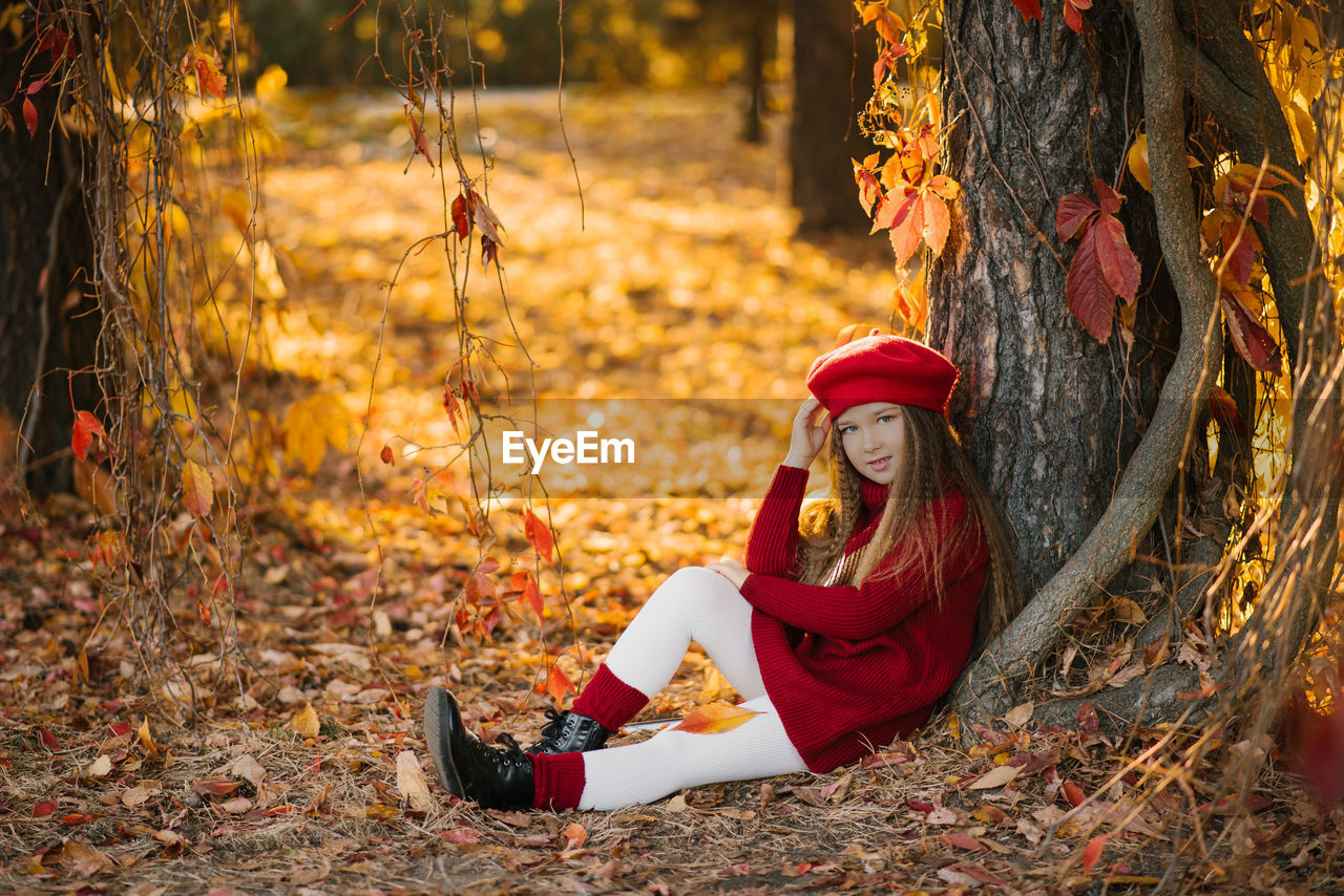 Happy child caucasian girl sitting near a tree in the park on a sunny day