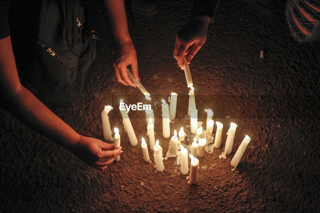 Cropped image of people igniting candles at night