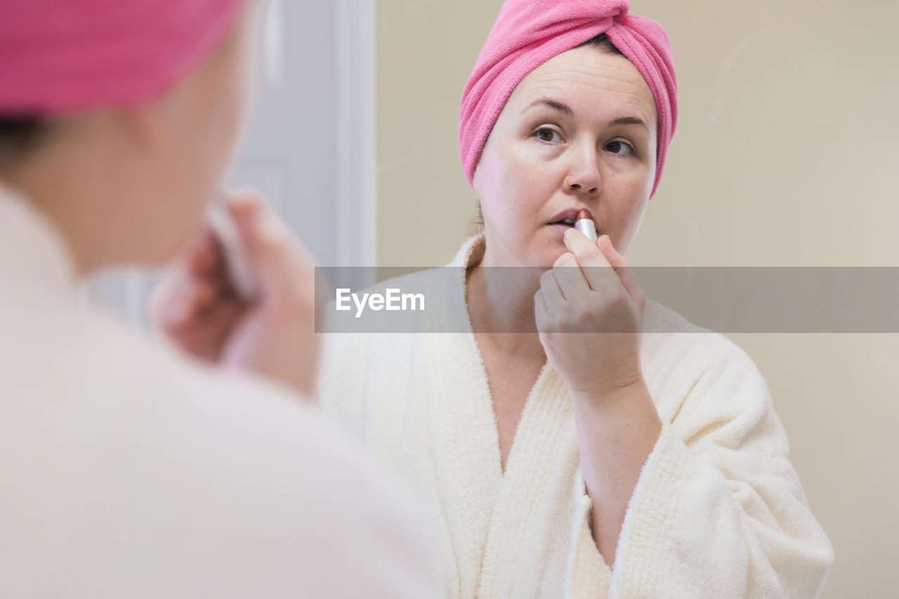 Mature woman applying lipstick reflecting on mirror