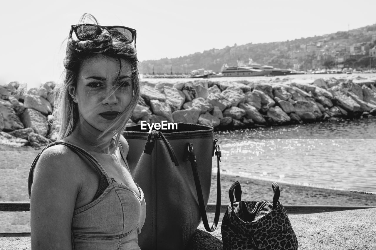 Close-up portrait of woman with purses on retaining wall against sea