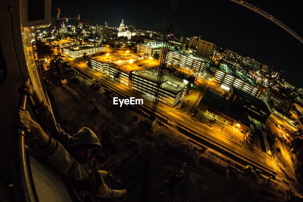 Man hanging from balcony with illuminated city in background