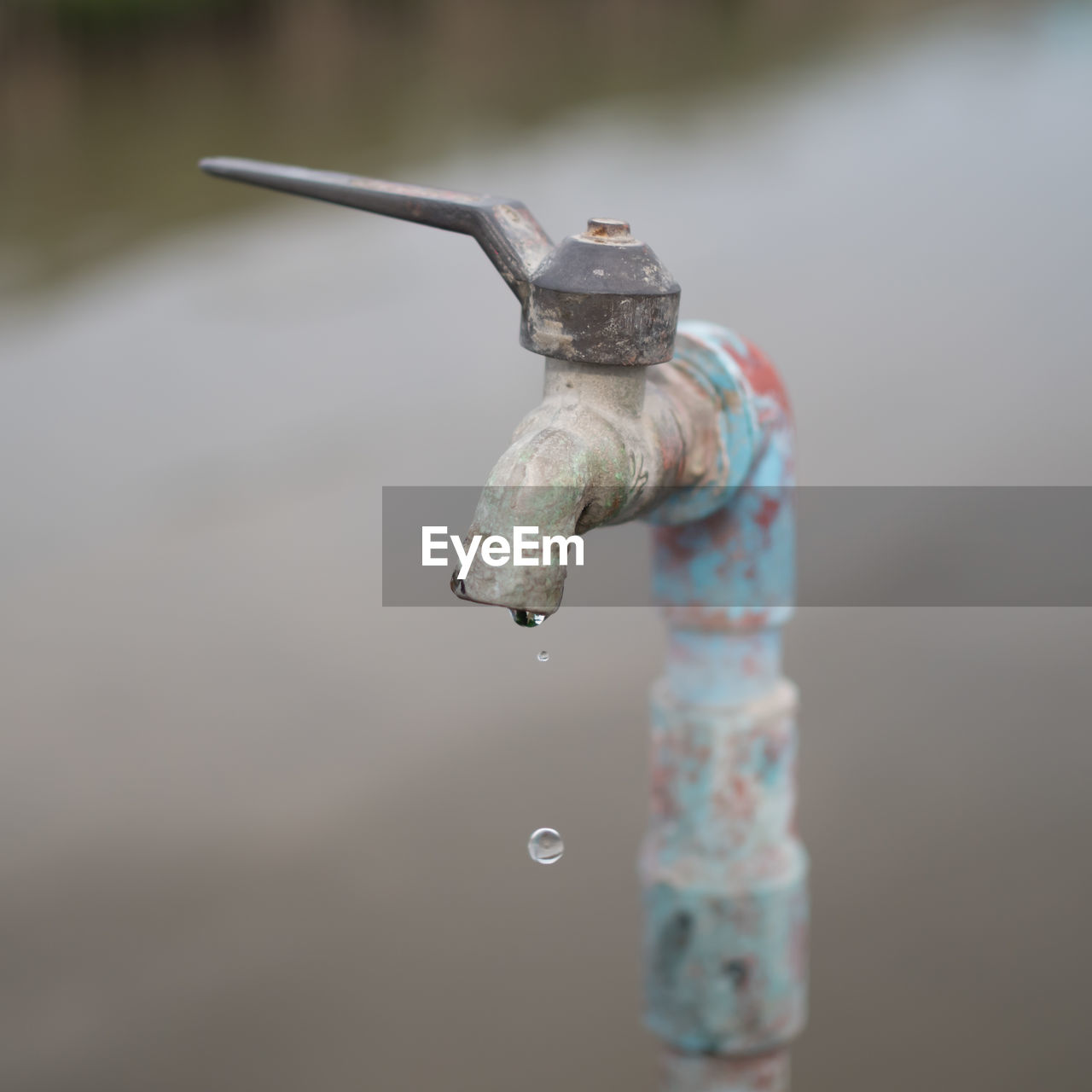 Close-up of water drop falling from metallic faucet