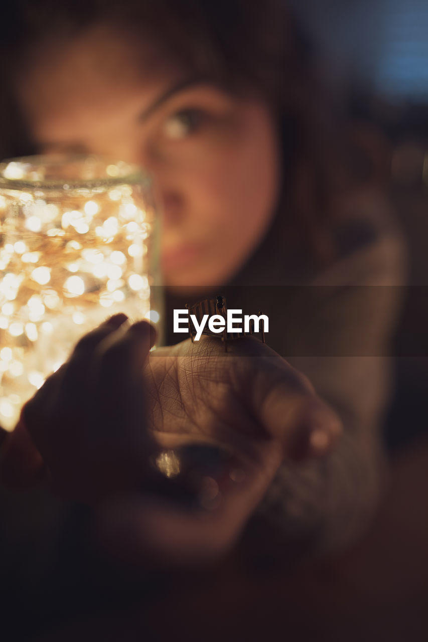 Portrait of woman holding illuminated lighting equipment in jar