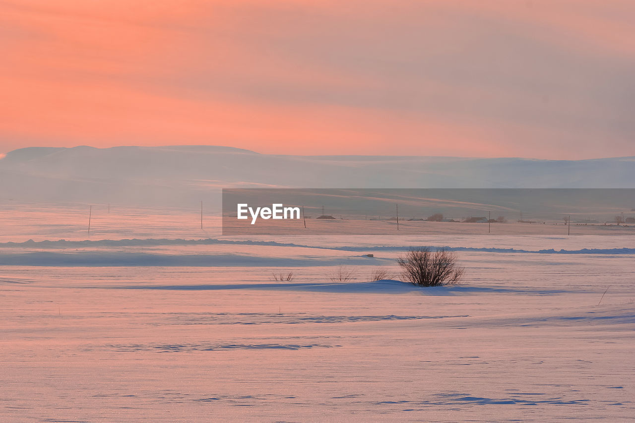 SCENIC VIEW OF SNOW COVERED FIELD AGAINST ORANGE SKY