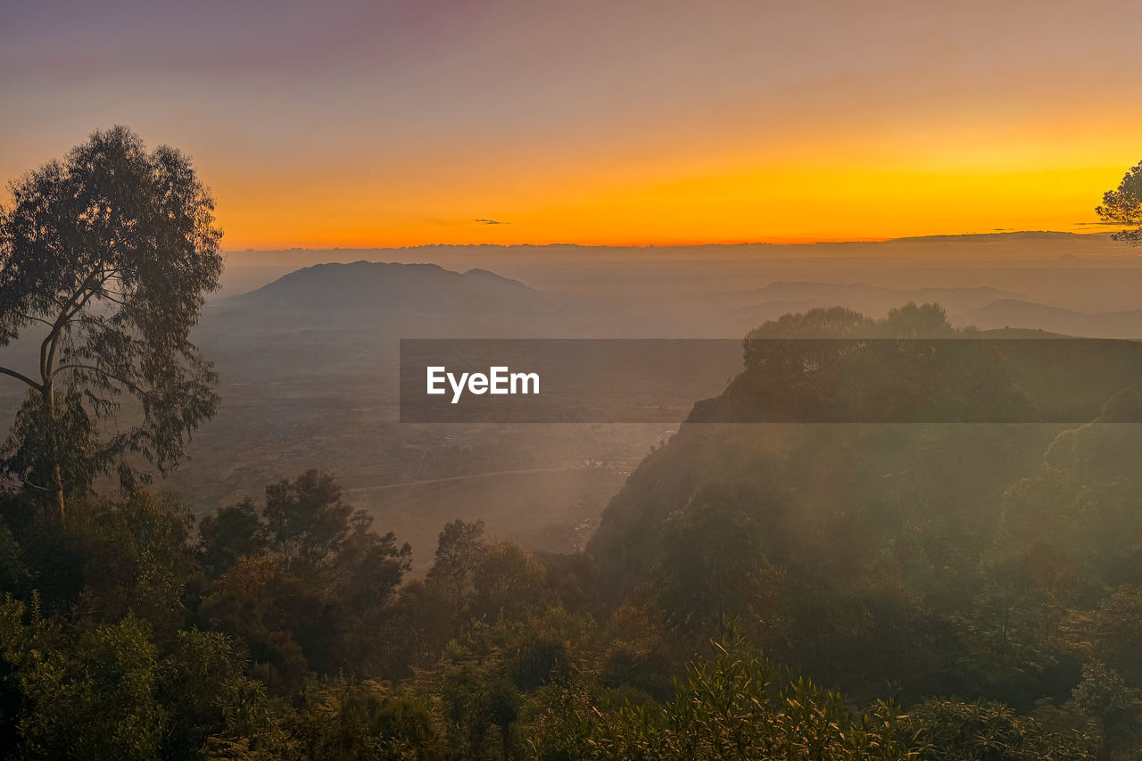 environment, morning, sunrise, landscape, sky, tree, nature, scenics - nature, fog, dawn, beauty in nature, plant, mountain, land, sun, travel, cloud, forest, mist, tranquility, travel destinations, sunlight, twilight, tourism, no people, orange color, outdoors, horizon, tranquil scene, mountain range, mountain peak, wilderness, rural scene, social issues, atmospheric mood, yellow, non-urban scene, vacation, trip, sunbeam, idyllic, holiday, multi colored, dramatic sky, valley, gold, summer, silhouette