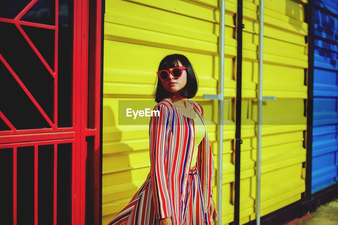 Young woman wearing sunglasses standing against building in city