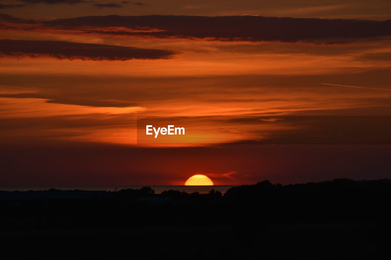 Silhouette field and river against cloudy sky during sunset