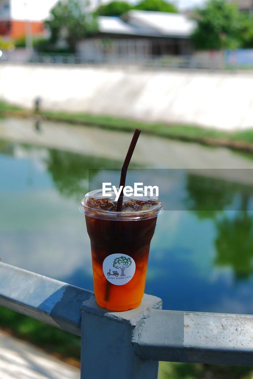 CLOSE-UP OF DRINK ON RAILING AGAINST LAKE