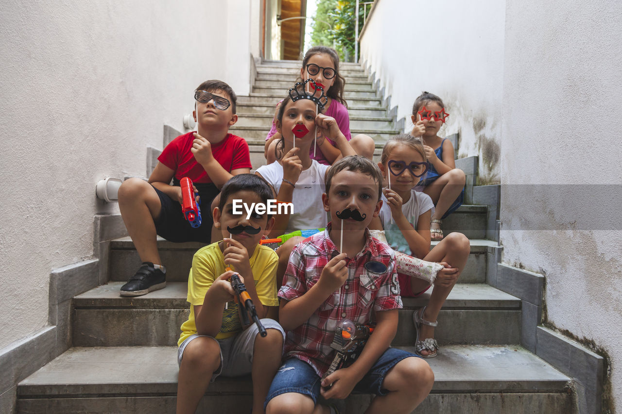 Group of little boys of different ages sitting on a stairway playing together with fun accessories