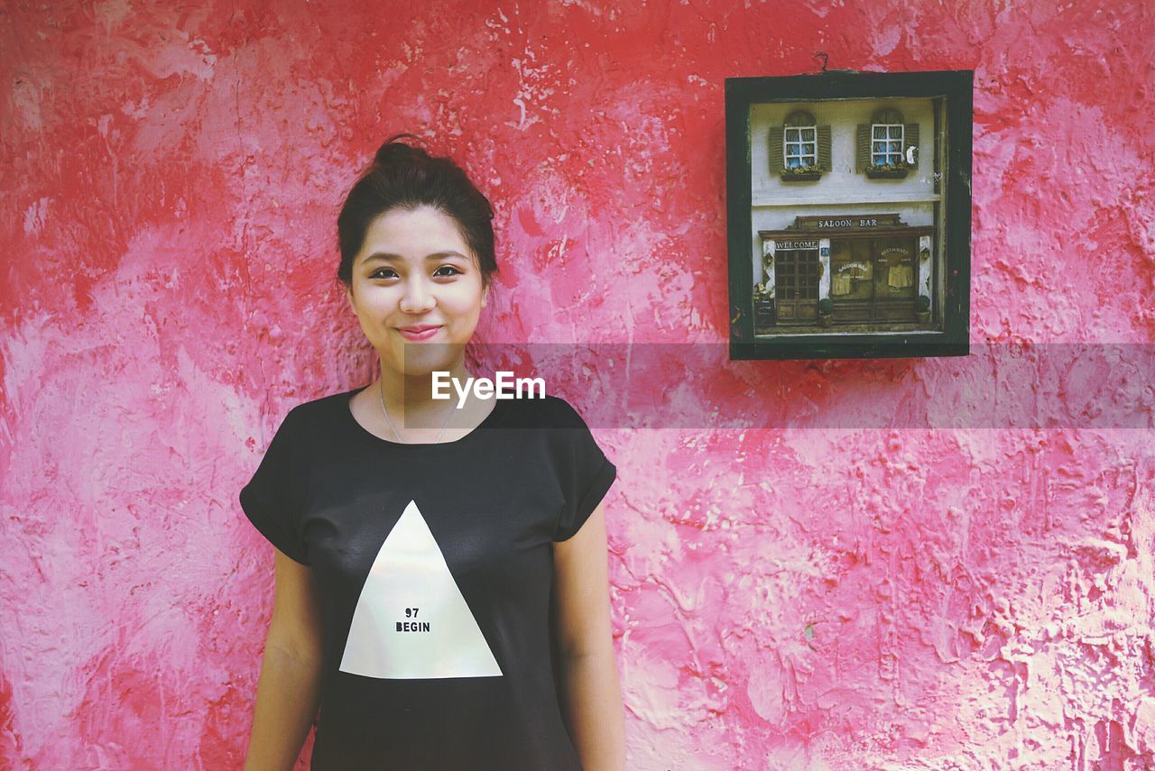 PORTRAIT OF YOUNG WOMAN AGAINST WALL