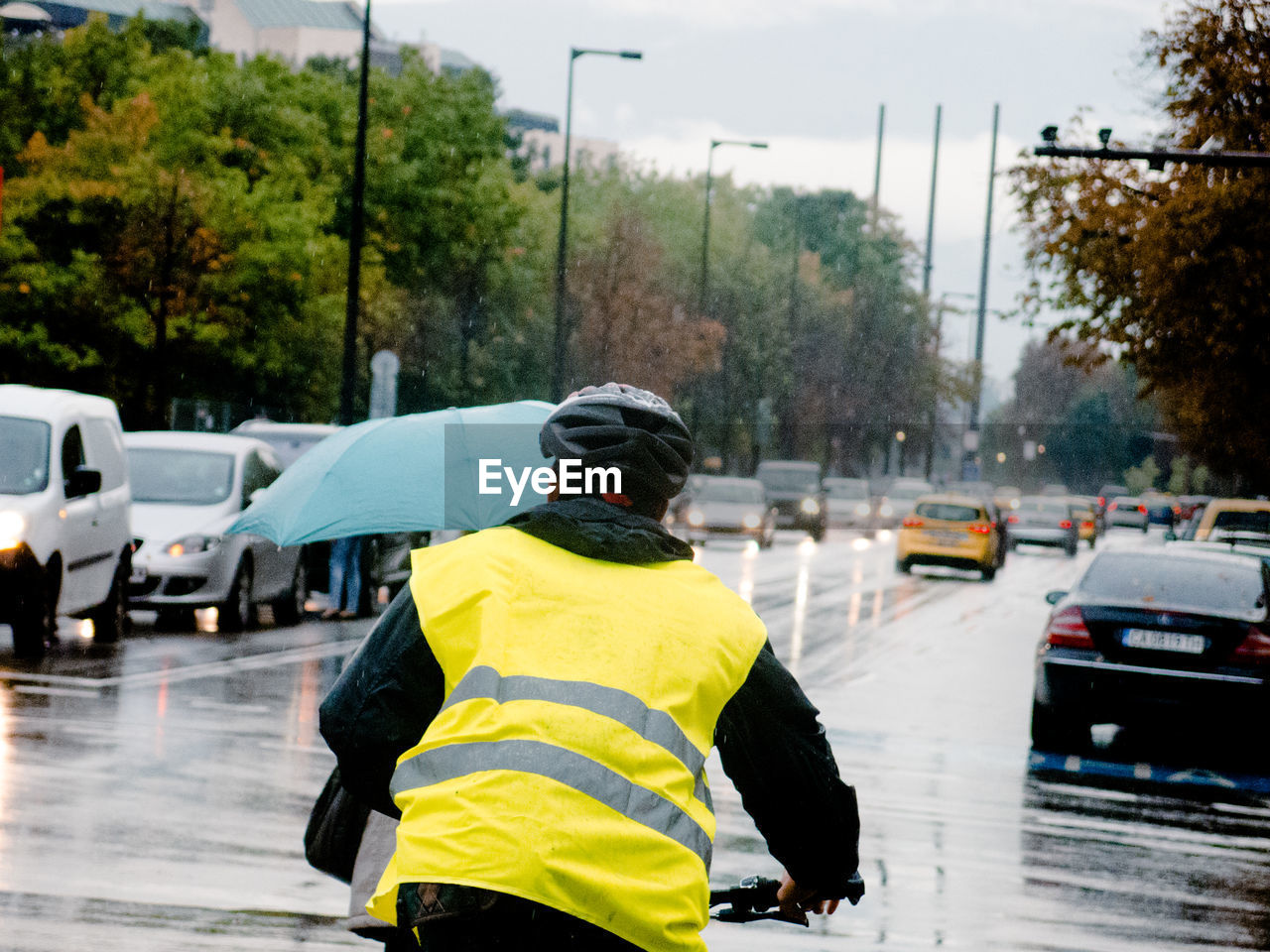 Rear view of man in reflective clothing cycling on wet city street