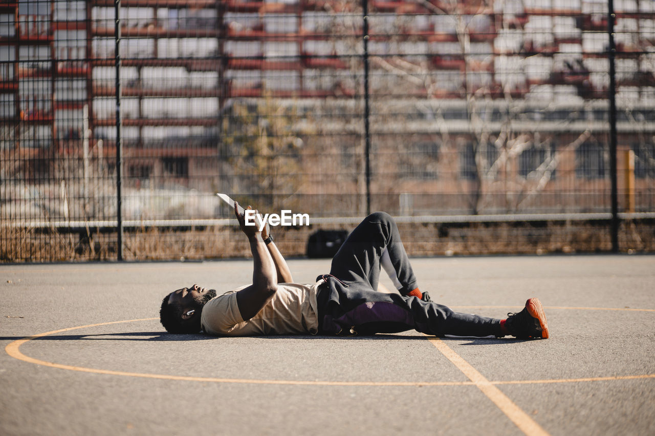 Young man using digital tablet while lying down on sports court during sunny day