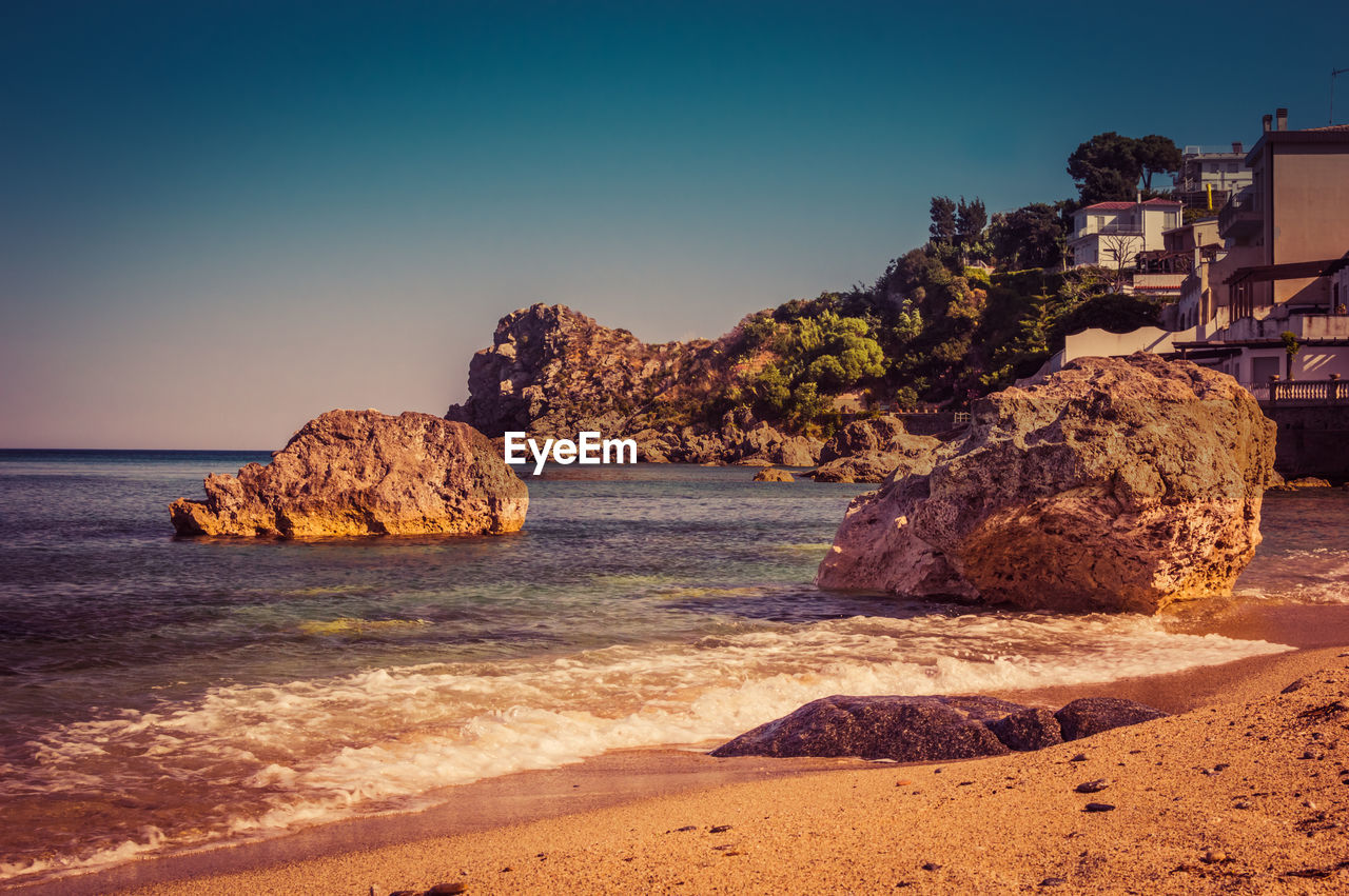 Rocks on beach against clear blue sky