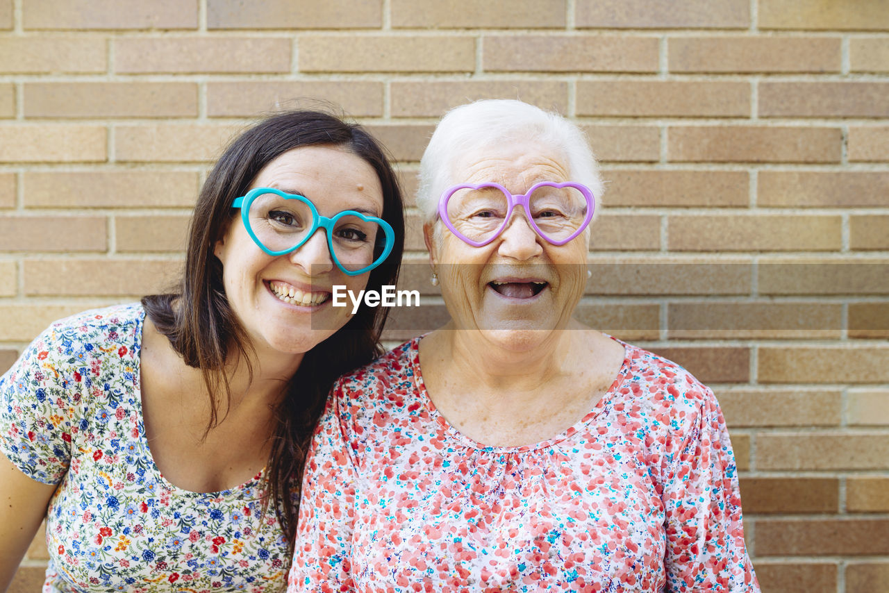 Happy granddaughter and grandmother wearing heart-shaped glasses