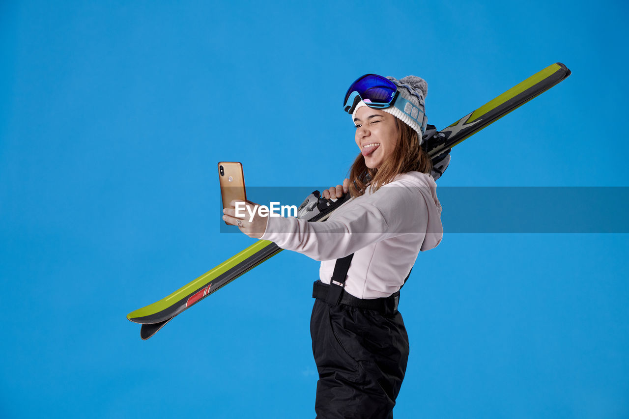 one person, blue, sports, adult, women, young adult, holding, happiness, copy space, emotion, smiling, clothing, nature, sky, glasses, fun, activity, motion, leisure activity, lifestyles, standing, female, athlete, clear sky, colored background, sunglasses