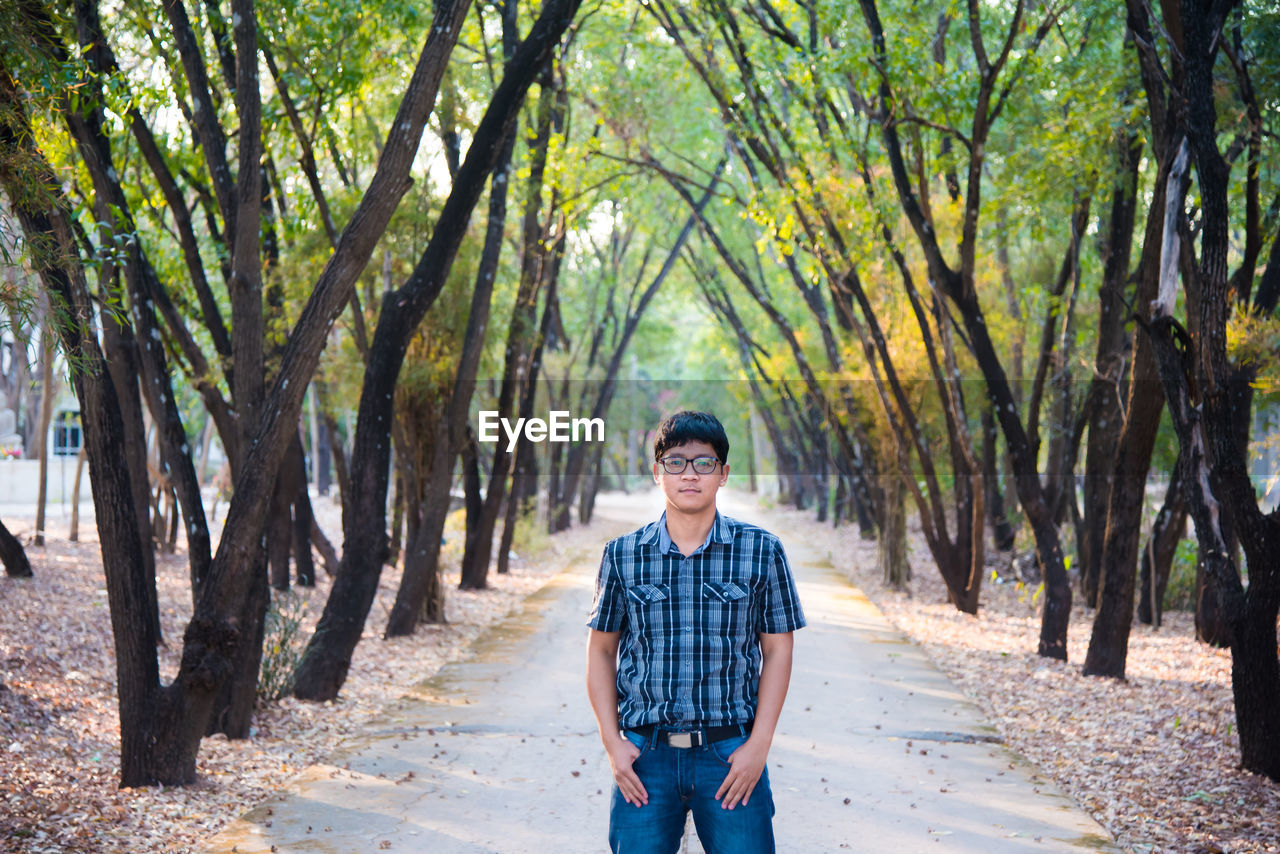 Portrait of young man standing on footpath at park