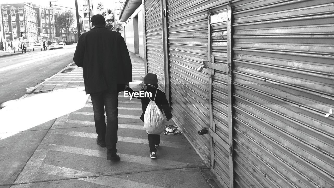 Rear view of father with son walking on sidewalk in city