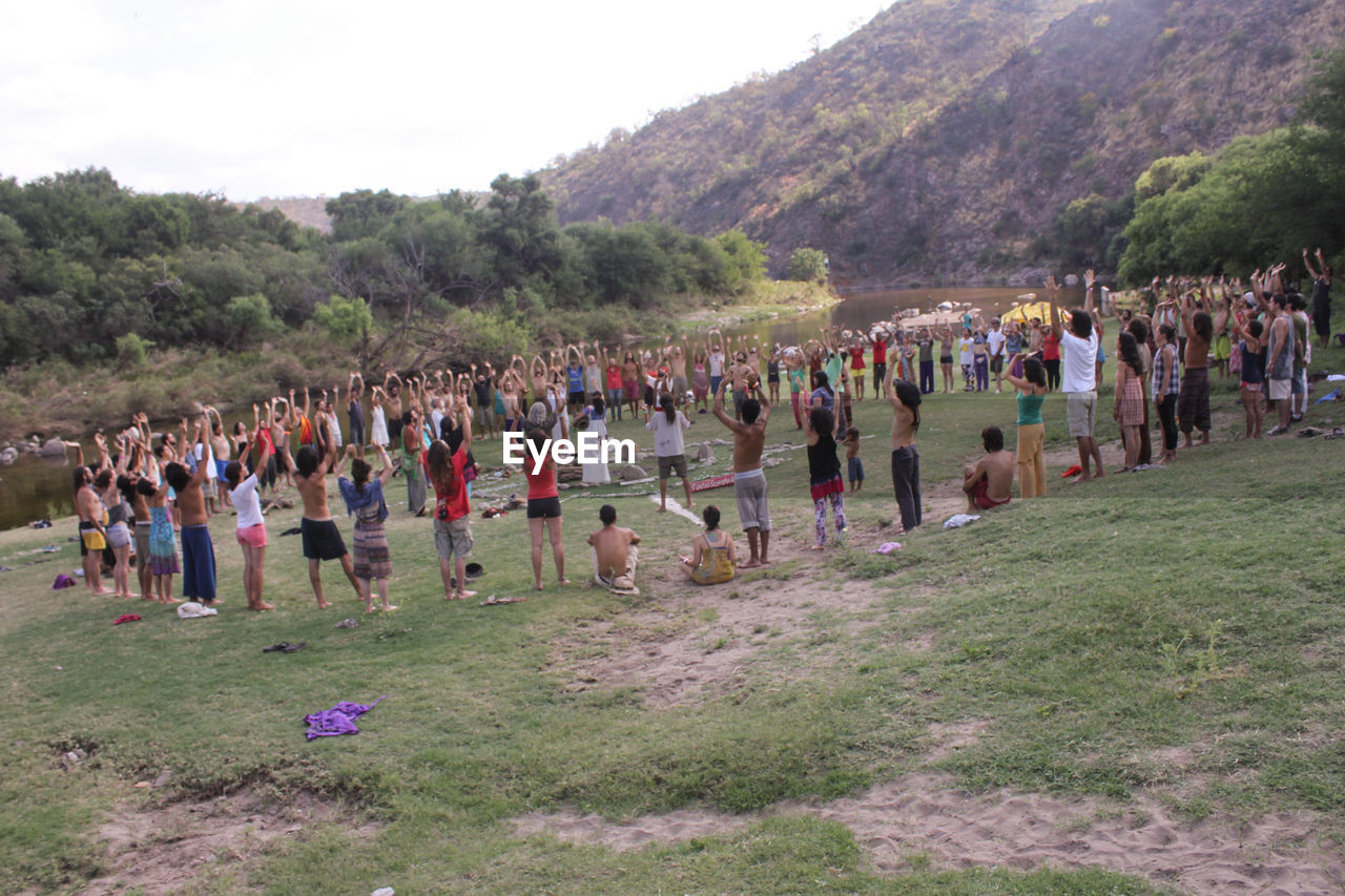 People standing with arms raised on grassy field during religious ceremony