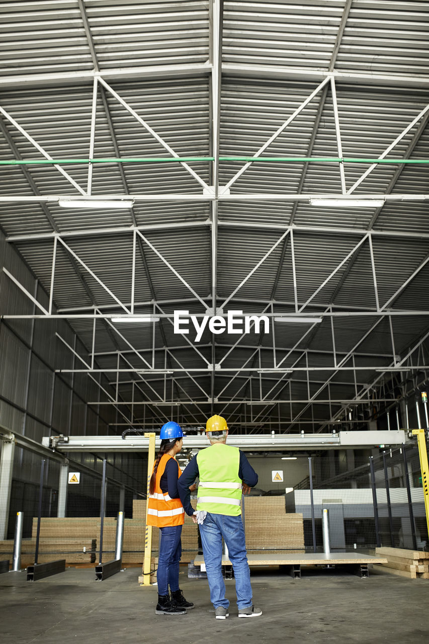 Rear view of male and female worker standing in factory workshop