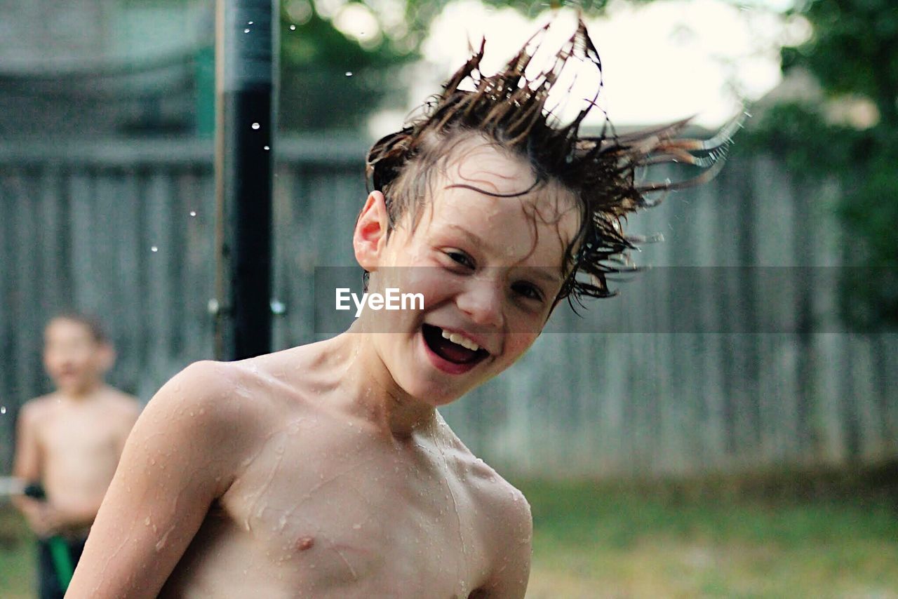 Close-up portrait of shirtless wet boy with tousled hair in backyard