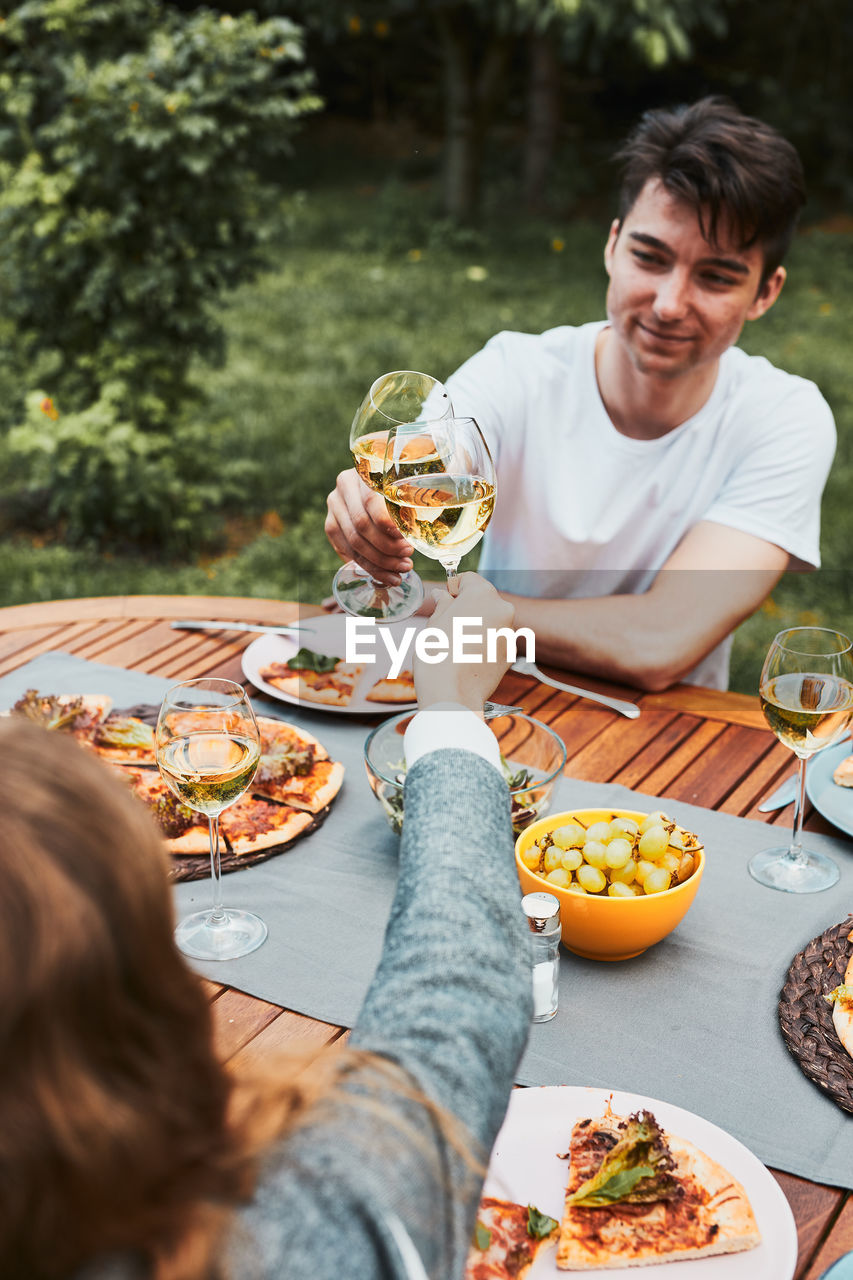 Friends making toast during summer picnic outdoor dinner in a home garden