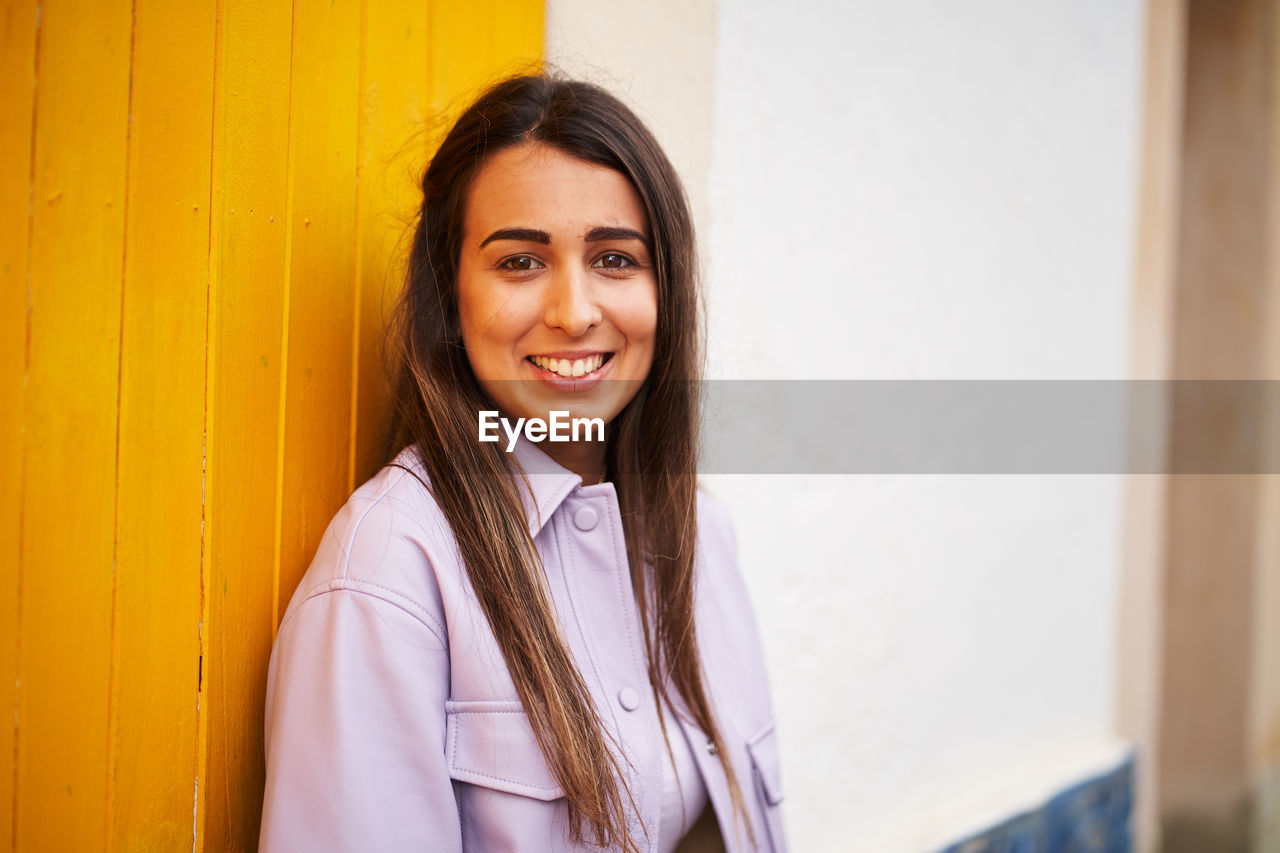 Portrait of smiling young woman against wall