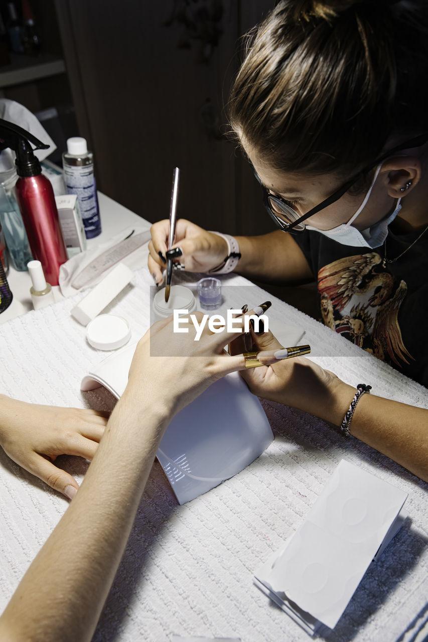 Woman in mask making french manicure to crop client during epidemic