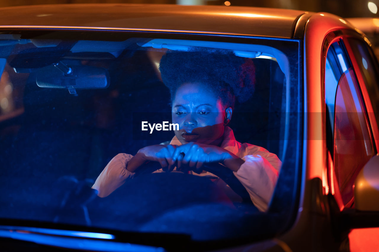 Depressed afro woman sit behind steering wheel in car at night, pondering about problems in life