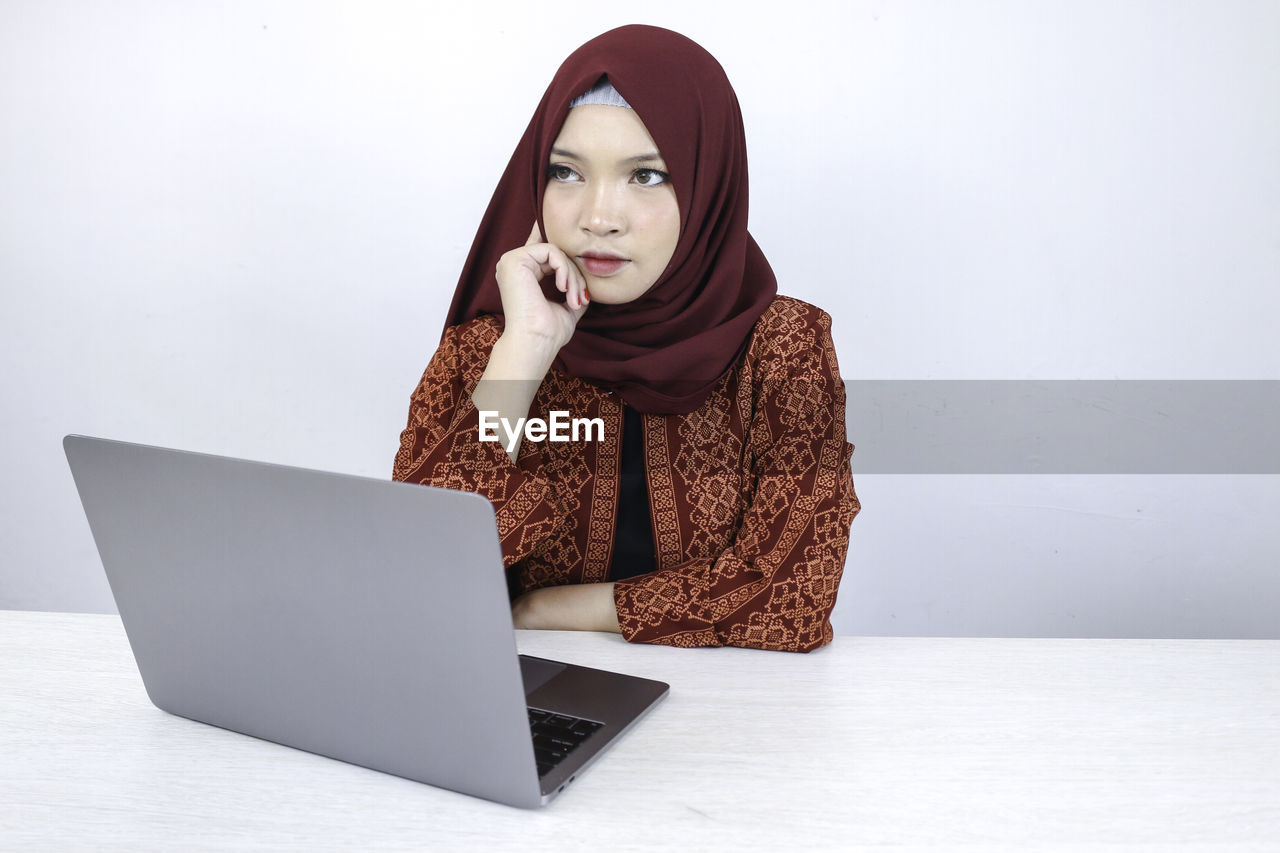 PORTRAIT OF YOUNG WOMAN USING SMART PHONE IN LAPTOP